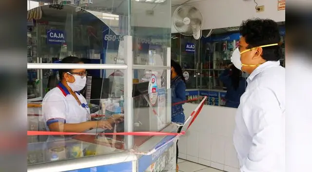 Las cajeras de las farmacias usan un vidrio para atender al cliente y usan un pedazo de cartón para recibir el dinero por el medicamento.