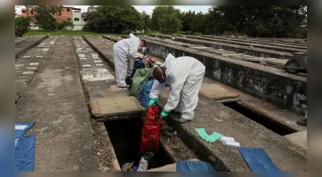 Los sepultureros con trajes protectores manipulan bolsas con huesos durante las exhumaciones en espacios abiertos sobre tumbas de cemento mientras se suspenden nuevos entierros.