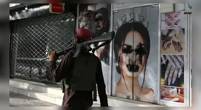 Un combatiente talibán pasa frente a un salón de belleza con imágenes de mujeres desfiguradas con pintura en aerosol en Shar-e-Naw, Kabul, el 18 de agosto de 2021. (Wakil KOHSAR / AFP). Un combatiente talibán pasa frente a un salón de belleza con imágenes de mujeres desfiguradas con pintura en aerosol en Shar-e-Naw, Kabul, el 18 de agosto de 2021. (Wakil KOHSAR / AFP).