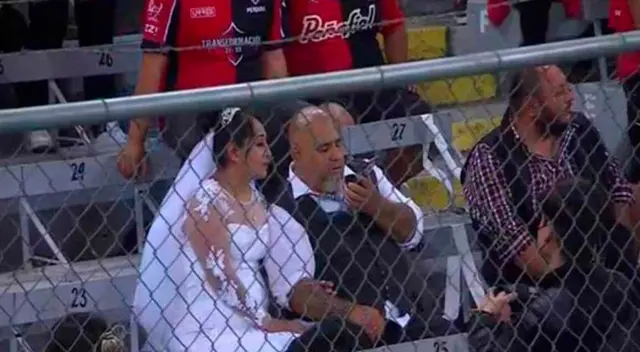 Recién casados asisten a un partido de futbol vestidos con sus trajes de matrimonio.