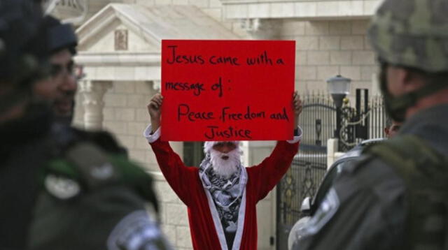 El mundo vide la Navidad desde distintos puntos de vista (manifestante vestido de Papá Noel protesta en enfrentamiento en Belén, Palestina)