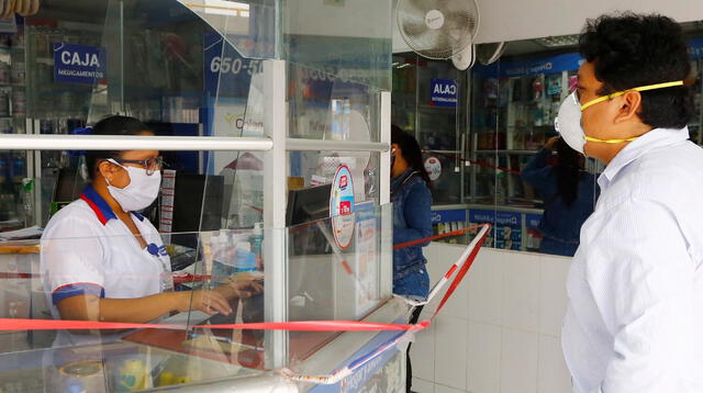 Las cajeras de las farmacias usan un vidrio para atender al cliente y usan un pedazo de cartón para recibir el dinero por el medicamento.