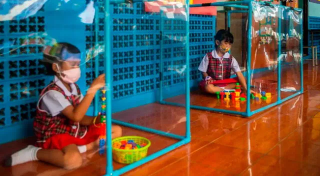 Dos alumnos tailandeses juegan detrás de pantallas de plástico en áreas de juego separadas en la escuela Wat Khlong Toey el 10 de agosto de 2020 en Bangkok, Tailandia.