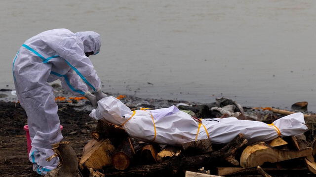 Un hombre junto al cadáver de un fallecido por COVID-19 antes de su cremación a orillas del río Ganges, en Garhmukteshwar (Uttar Pradesh, la India), el 6 de mayo de 2021.